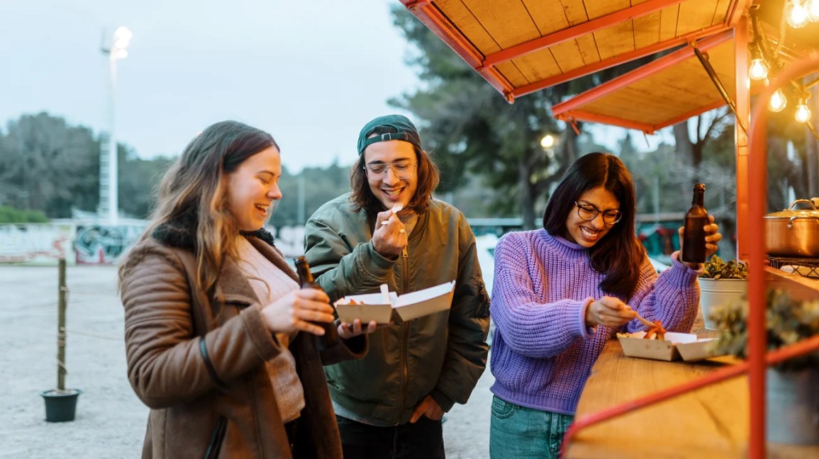 Three friends enjoy a meal outdoors at a food truck together.