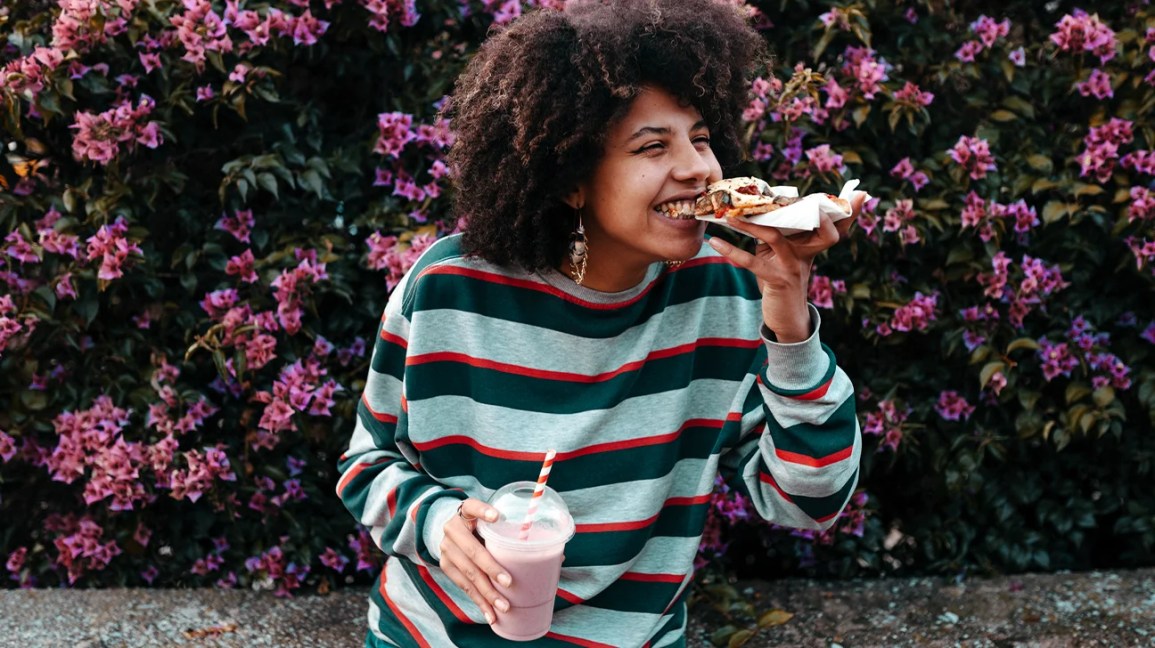 person smiles with pleasure as they bite into a pizza